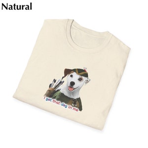 May include: Cream-colored t-shirt featuring a dog dressed as a hunter with a quiver of arrows. The dog wears a green and brown hat and vest. Text on the shirt reads "I got that dog in me" in red, blue, and pink.