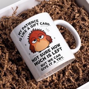 Pode incluir: Caneca de cerâmica branca com um design humorístico. A caneca apresenta um pássaro de desenho animado com uma expressão carrancuda e o texto "My patience is like a gift card. Not sure how much is left but we can give it a try."