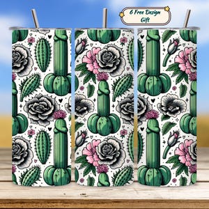 Op de afbeelding: Drie roestvrijstalen bekers met een herhalend patroon van groene cactussen en roze en zwarte rozen op een witte achtergrond. Elke beker heeft een zilveren rietje en een deksel. De bekers staan op een houten oppervlak.