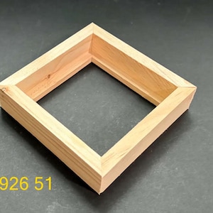 May include: A square wooden frame with a natural light brown finish and visible wood grain. The frame features mitered corners and a recessed inner edge. The numbers 926 51 are printed in yellow in the lower left corner of the image.