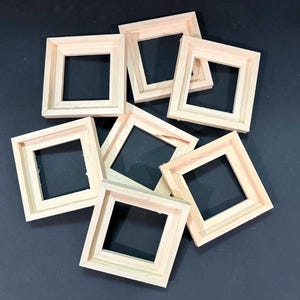 May include: A collection of six square, unfinished light-colored wooden frames arranged in a cluster. Each frame features a simple, clean-lined design with a flat profile and a hollow center, showcasing the natural grain and texture of the wood.