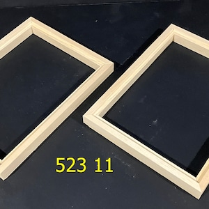 May include: Two unfinished wooden picture frames with a rectangular shape. The frames are made of light-colored wood and have a simple, clean design. The number "523 11" is printed in yellow on the bottom of the image. The frames are set against a dark background.