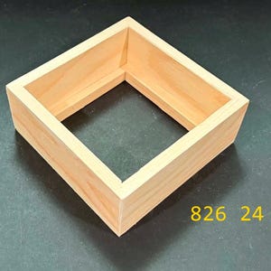May include: A square, light-colored wooden frame with an open center and straight sides. The frame features a natural wood grain texture and a smooth finish. The yellow text 826 24 is visible in the lower right corner of the image.