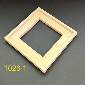 May include: A square, light-colored wooden frame with mitered corners and a recessed inner edge. The frame is positioned at an angle, and the yellow text '1026 1' is printed in the lower left corner of the image area.