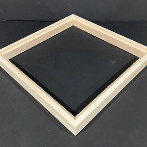 May include: A light-colored, unfinished wooden frame in a diamond shape. The frame is constructed from rectangular pieces of wood joined at the corners. The frame is designed to hold a canvas or artwork.