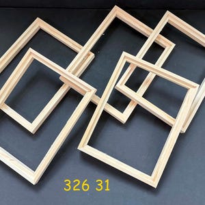 May include: A collection of six unfinished, rectangular wooden frames. The frames are made of light-colored wood and are arranged at various angles against a dark background. The number "326 31" is printed in yellow.