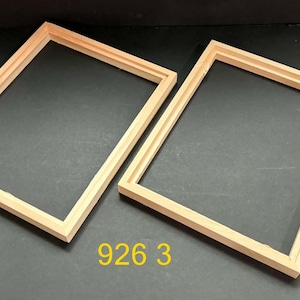May include: Two rectangular light-colored wooden frames with a simple profile. The frames are empty and feature a clean, natural wood grain finish. The number 926 3 is printed in yellow text between the two frames on the dark surface.