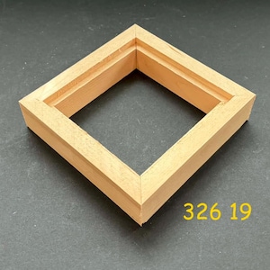 May include: A square, light-colored wooden frame with mitered corners. The frame has a recessed inner edge. The number "326 19" is printed in yellow on the lower right corner. The frame is likely for artwork or a similar display.