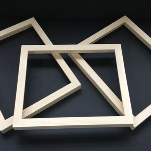 May include: Three unfinished wooden picture frames of different sizes, stacked on top of each other. The frames are made of natural wood and have a smooth finish.