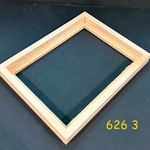 May include: A rectangular light-colored wooden frame with mitered corners and a recessed inner edge. The frame has a natural wood grain finish and is positioned at an angle. The yellow text 626 3 is visible in the lower right corner of the image.