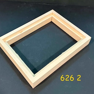 May include: A rectangular light-colored wooden frame with a stepped inner edge profile. The frame has a natural wood grain finish and is displayed at an angle. The yellow text 626 2 is visible in the lower right corner of the image.