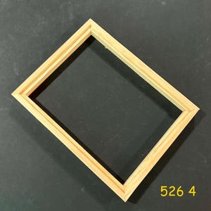 May include: A rectangular, unfinished wooden picture frame with a double-layered design. The frame is made of light-colored wood and is empty, with the number "526 4" printed in yellow in the lower right corner. The frame is set against a dark background.