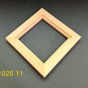 May include: A square wooden picture frame with a light tan natural wood grain finish, positioned at a diamond angle. The frame features a stepped inner edge profile and the yellow text 1026 11 is printed in the bottom left corner of the image.