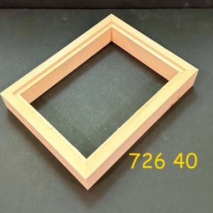 May include: A rectangular light-colored wooden picture frame with a stepped inner edge profile. The frame has mitered corners and a natural wood grain finish. The yellow text 726 40 is printed near the bottom right corner of the frame structure.