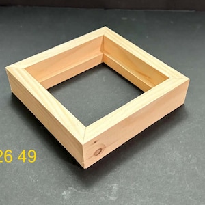 May include: A square wooden frame with a light tan natural wood grain finish and mitered corners. The frame has a hollow center and a visible wood knot on the front lower right side. The yellow text 926 49 is printed on the lower left side.