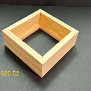 May include: A square, light-colored wooden frame with mitered corners and a hollow center. The natural wood grain is visible throughout the structure. The yellow text 926 52 is printed in the lower left corner of the image, outside the frame.