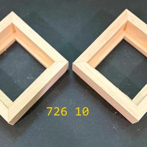 May include: Two square, light-colored wooden frames with mitered corners and a hollow center. The frames are positioned side-by-side, and the text 726 10 is printed in yellow between them. The frames have a natural wood grain finish.
