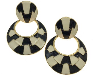 May include: A pair of black and white geometric dangle earrings with gold accents. The earrings feature a circular design with a smaller circle on top.