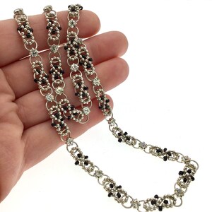 May include: A silver chain necklace featuring black beads and clear rhinestones. The chain is crafted from small, interlinked rings.