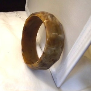 K&ouml;nnte beinhalten: Ein facettiertes, bernsteinfarbenes Armreif-Armband. Das Armband hat eine glatte, polierte Oberfl&auml;che und ein geometrisches Design. Die warmen Farbt&ouml;ne des Armbands deuten darauf hin, dass es aus einem nat&uuml;rlichen Material besteht. Das Armband ist ein Schmuckst&uuml;ck.