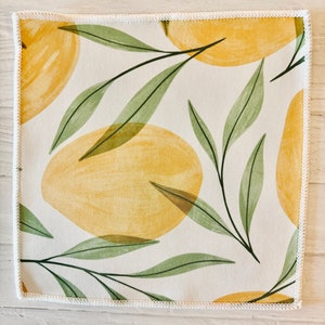 May include: A white fabric square with a yellow and green pattern. The pattern features stylized lemons and leaves. The fabric has a white stitched border.