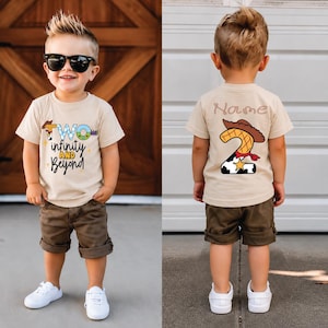 Puede incluir: Una camiseta beige de manga corta con estampado gráfico. El frente muestra el texto "TWO infinity AND Beyond" con un sombrero de vaquero y una estrella de sheriff. La parte posterior muestra un número "2" grande con un sombrero y "Name".