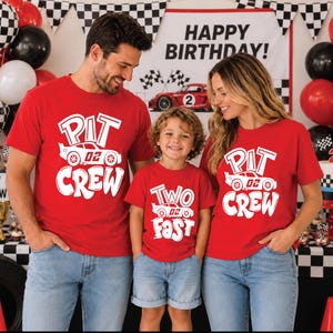 May include: Three red short-sleeve t-shirts featuring white graphic prints. Two shirts display the text PIT CREW with a race car graphic, while the smaller shirt displays the text TWO FAST with a race car graphic, all in a bold, stylized font.