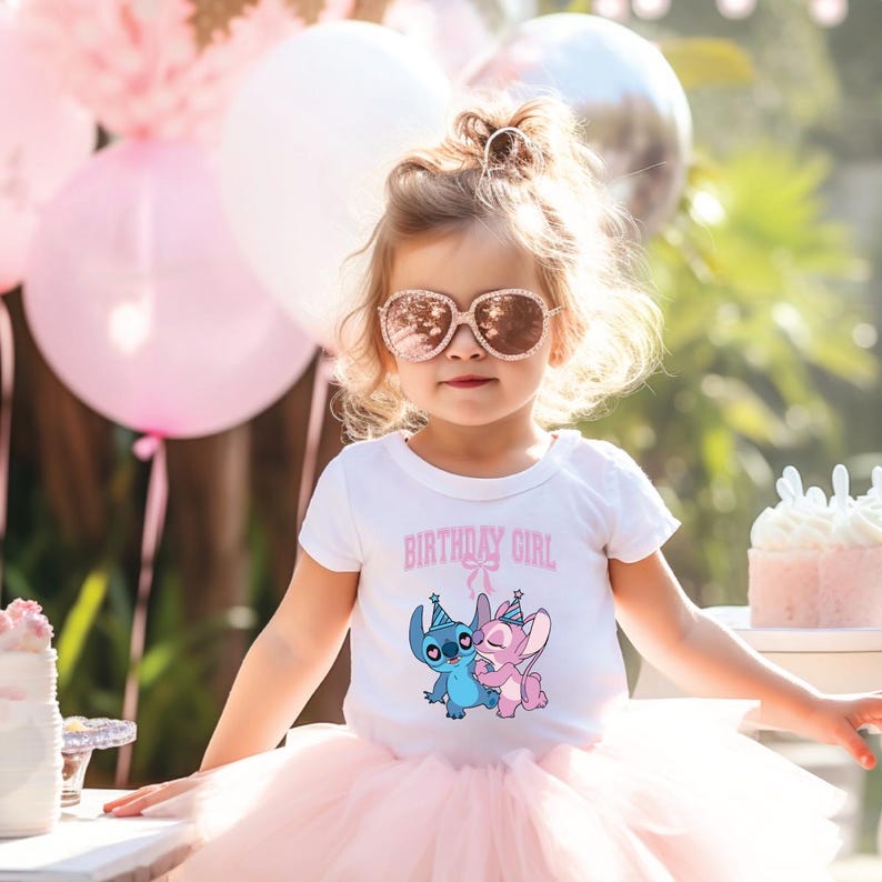 May include: A young child wearing a white t-shirt with the text "BIRTHDAY GIRL" and a cartoon graphic of Stitch and Angel. The child is also wearing a pink tutu, rose-colored sunglasses, and has a hair accessory. Pink balloons and a cake are in the background.