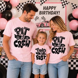May include: Three light pink t-shirts featuring black graphic prints. Two shirts display the text "PIT CREW" with a race car illustration, while the smaller shirt displays the text "TWO FAST" with a race car illustration.