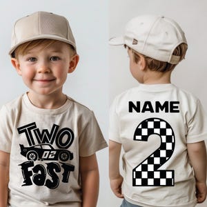 May include: A beige t-shirt featuring a black graphic of a race car with the text Two Fast on the front and the word NAME above a large checkered number 2 on the back, paired with a matching beige baseball cap worn by a young child.