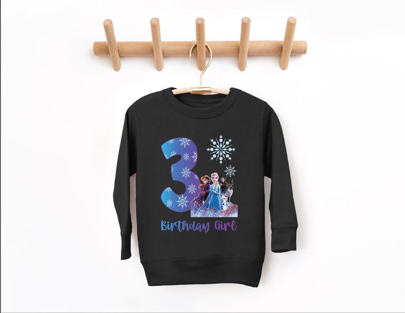 Pode incluir: Camisola preta de manga comprida com um n&uacute;mero 3 azul e roxo e detalhes de flocos de neve. A camisola tem um gr&aacute;fico de personagens animados e o texto "Birthday Girl" em roxo.