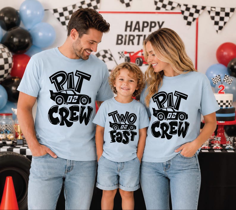 May include: Light blue t-shirts featuring black graphic prints. Two shirts display the text PIT CREW with a race car illustration labeled 02. One shirt displays the text TWO FAST with a race car illustration labeled 02. The shirts are short-sleeved.