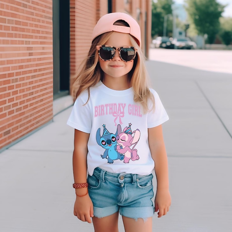 May include: A young girl wearing a white t-shirt with the text "BIRTHDAY GIRL" in pink. The shirt features a cartoon image of two characters. She is also wearing denim shorts, a pink cap, and sunglasses.