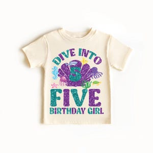 Puede incluir: Una camiseta blanca con un diseño de purpurina morado y turquesa que dice "Dive into Five Birthday Girl". El diseño presenta una concha con un número cinco en su interior, rodeado de criaturas marinas como una estrella de mar, un caballito de mar y un pulpo.