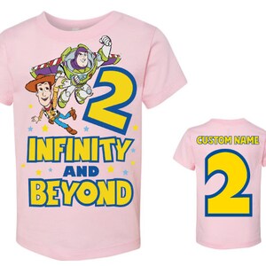 Op de afbeelding: Roze T-shirt met een cartoon afbeelding van Buzz Lightyear en Woody uit Toy Story. Het shirt staat "2 Infinity and Beyond".