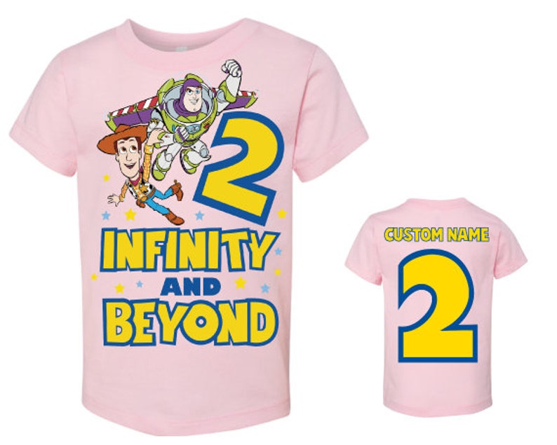 Op de afbeelding: Roze T-shirt met een cartoon afbeelding van Buzz Lightyear en Woody uit Toy Story. Het shirt staat "2 Infinity and Beyond".