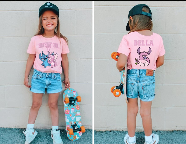 May include: A young girl wearing a pink t-shirt with the text "BIRTHDAY GIRL" and a cartoon graphic of Stitch and Angel. She is also wearing denim shorts, a black cap, and holding a skateboard with a colorful design.