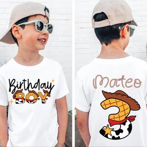 May include: White t-shirt with "Birthday Boy" text and cowboy-themed graphics. The back of the shirt has the name "Mateo" and a number 3 with a cowboy hat and sheriff's badge. The shirt is designed for a child's birthday.
