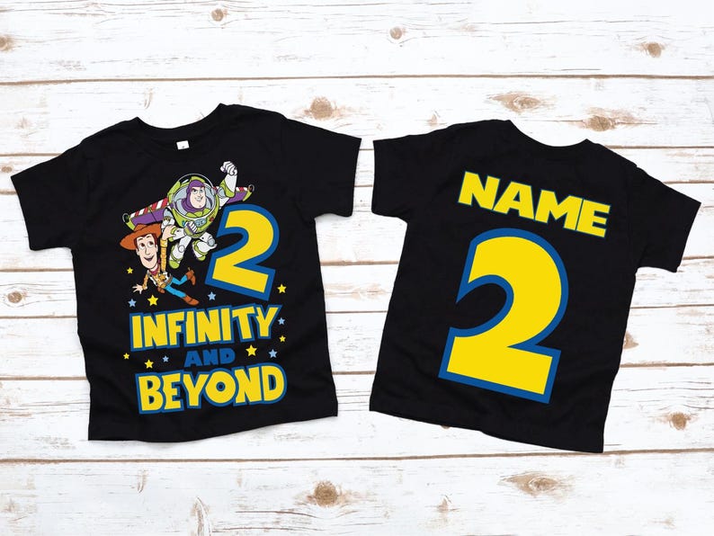 Op de afbeelding: Twee zwarte T-shirts met een Toy Story-thema. E&eacute;n shirt heeft Woody en Buzz Lightyear met het nummer 2 en de tekst "Oneindig en verder". Het andere shirt heeft het nummer 2 en het woord "NAME" in een blauwe omtrek.