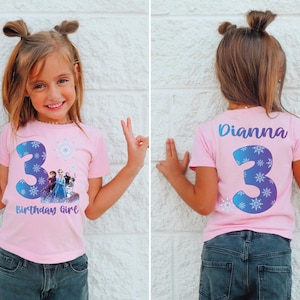Pode incluir: Uma t-shirt rosa com o n&uacute;mero 3 azul e detalhes de flocos de neve, com personagens de um filme de anima&ccedil;&atilde;o popular. A t-shirt tamb&eacute;m tem o texto "Birthday Girl". A parte de tr&aacute;s da t-shirt tem o nome "Dianna" e o n&uacute;mero 3.