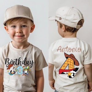 Op de afbeelding: Een beige T-shirt met een zwarte "Birthday Boy" afbeelding met Toy Story-personages. De achterkant van het shirt heeft een beige nummer 4 met een cowboyhoed en de naam "Antonio" in bruine tekst.