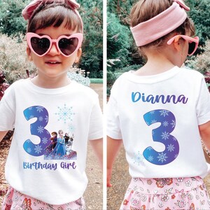Pode incluir: Uma camiseta branca com o n&uacute;mero 3 azul e design de floco de neve, com personagens do filme Frozen. O texto "Birthday Girl" est&aacute; abaixo do n&uacute;mero. A parte de tr&aacute;s da camisa tem o nome "Dianna" e o n&uacute;mero 3.