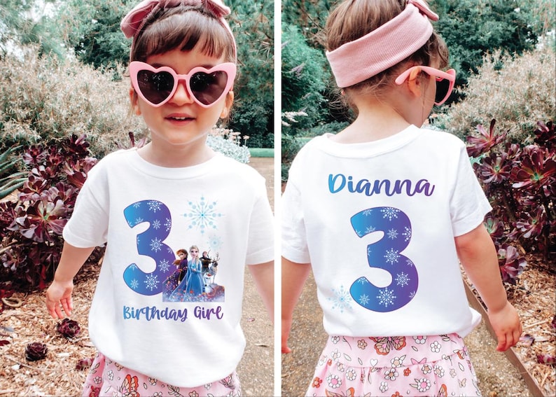 Pode incluir: Uma camiseta branca com o n&uacute;mero 3 azul e design de floco de neve, com personagens do filme Frozen. O texto "Birthday Girl" est&aacute; abaixo do n&uacute;mero. A parte de tr&aacute;s da camisa tem o nome "Dianna" e o n&uacute;mero 3.
