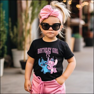 May include: A young child wearing a black t-shirt with the words "BIRTHDAY GIRL" in pink, along with a cartoon graphic of two characters. The child is also wearing a pink headband with a bow and black sunglasses. The child is wearing pink pants.