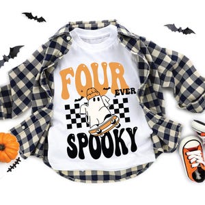 May include: White t-shirt with the words "FOUR EVER SPOOKY" in orange and black, featuring a ghost on a skateboard. The shirt is layered with a blue and white plaid shirt and orange sneakers. Halloween-themed.
