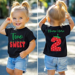 May include: A black t-shirt with the text "Two Sweet" in green letters and strawberry graphics. The back of the shirt has a strawberry graphic with the number "2" inside and the text "Name Here".