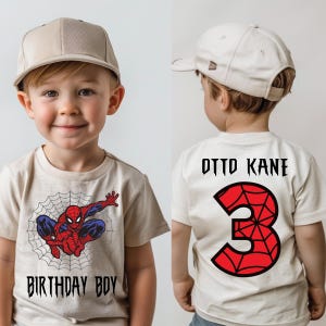 Peut inclure: Un t-shirt beige avec un motif Spiderman et le texte "Birthday Boy" sur le devant. Le dos du t-shirt porte le texte "Otto Kane" et un chiffre 3 rouge avec un motif de toile d'araignée.