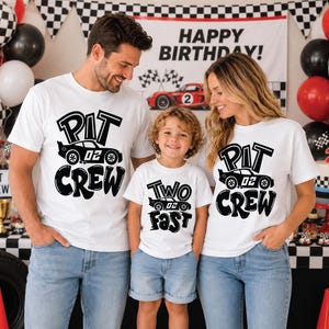 May include: Three white t-shirts featuring black graphic prints. Two shirts display the text PIT CREW with a race car graphic, while the smaller shirt displays the text TWO FAST with a race car graphic. All shirts feature the number 02 on the cars.