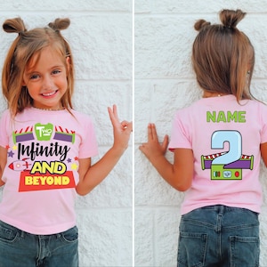 Puede incluir: Camiseta rosa con el texto "Infinity and Beyond" y un gráfico de cohete. La parte trasera de la camiseta tiene el número "2" y la palabra "Name". La camiseta la lleva un niño.