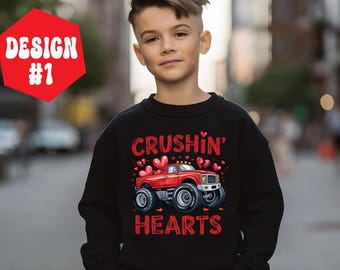 May include: Black sweatshirt featuring a red monster truck graphic and the words "Crushin' Hearts" in red. The truck has large tyres and is decorated with hearts. A red hexagon with "Design #1" in white is in the upper left corner.
